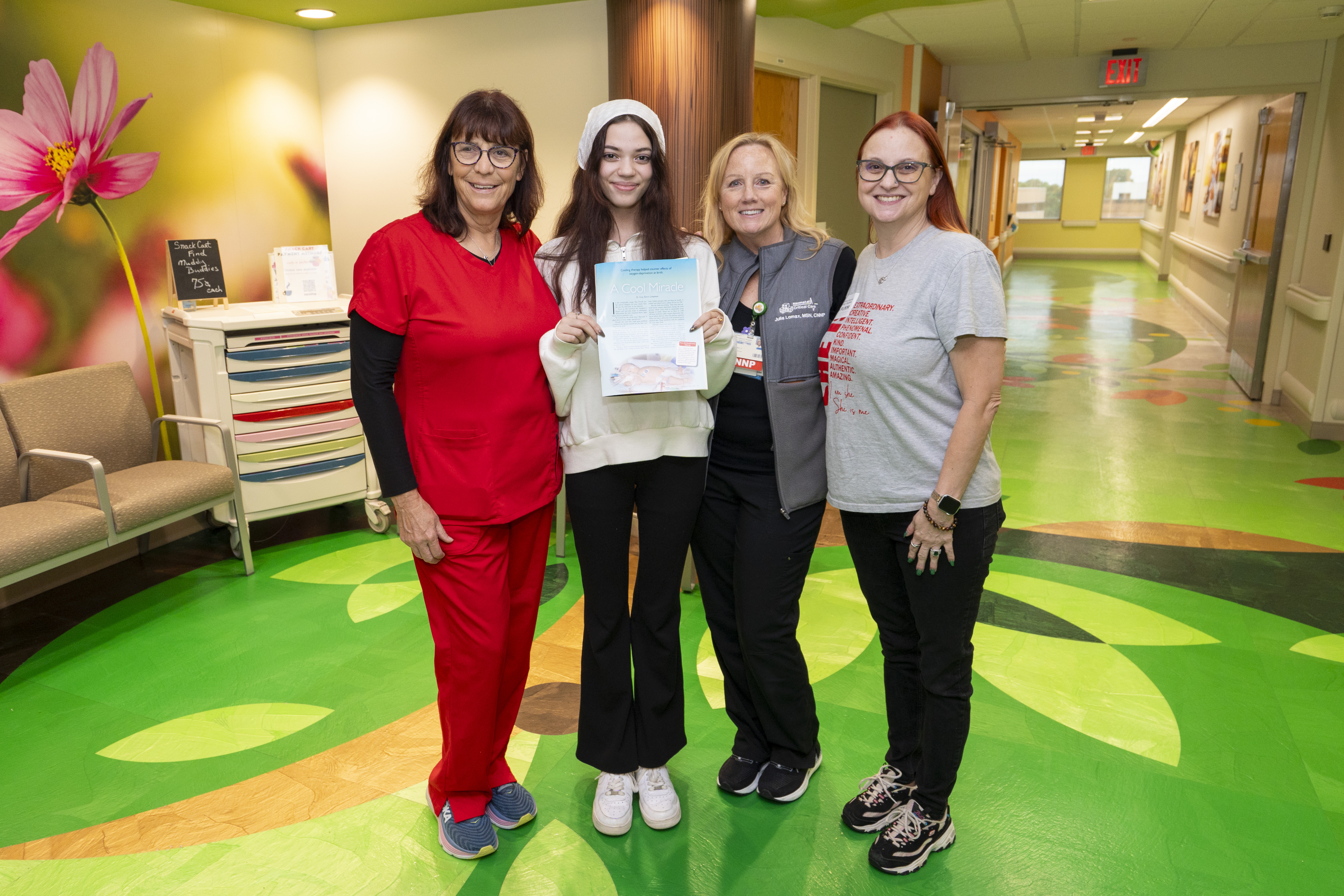 Nai’lah Powell shows off her KidStuff feature from 18 years ago, celebrating with former NICU care team members nurse MaryBeth Sanders, neonatal nurse practitioner Julia Lomax, and her mom, Rita Powell.