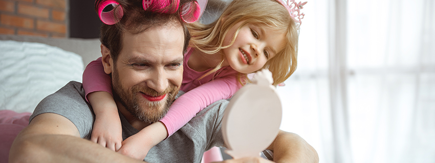 Father, wearing lipstick and hair curlers, carries daughter on shoulders. 