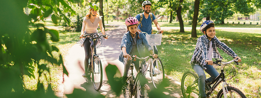 Family of four rides bikes in the park.