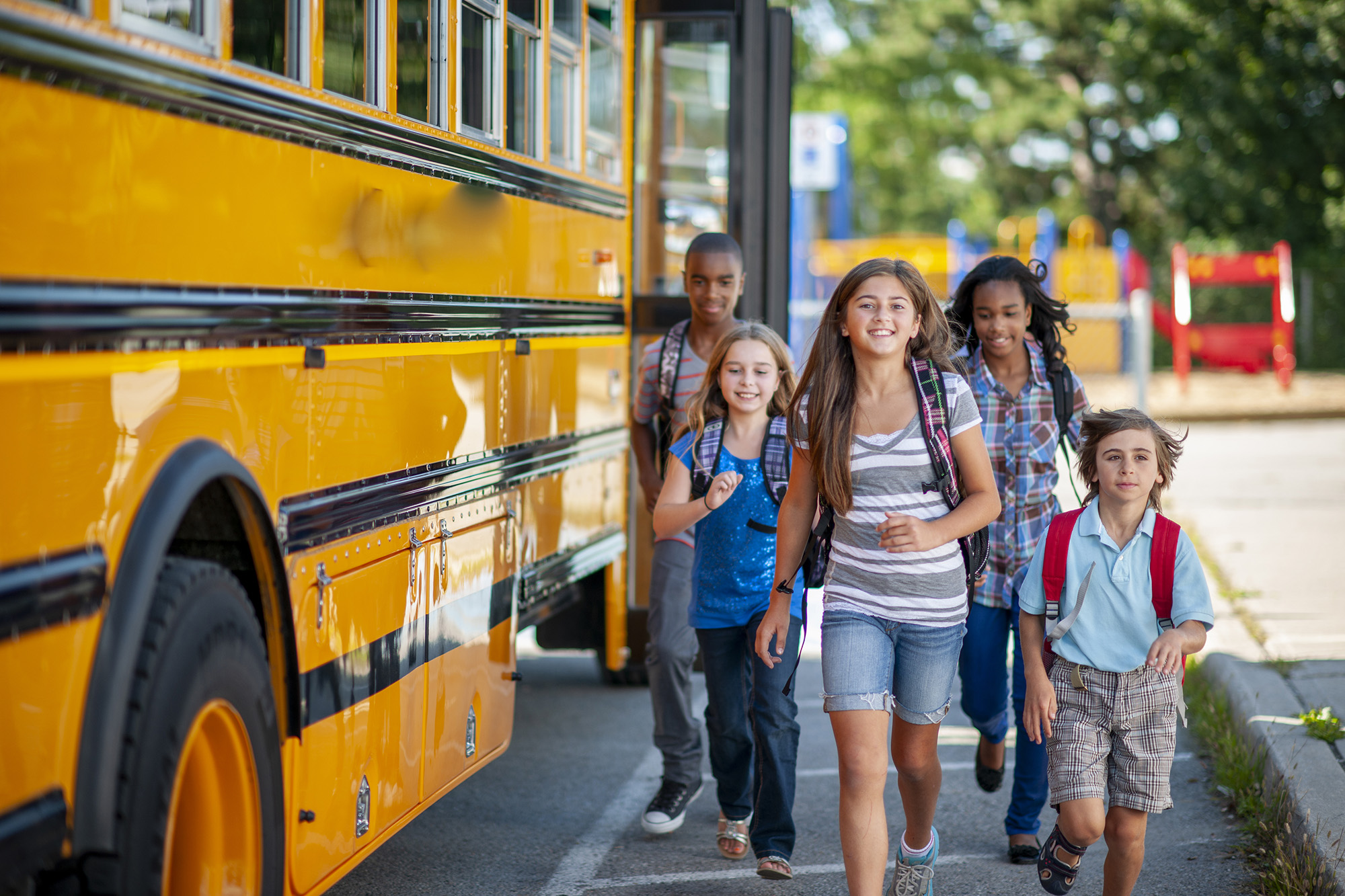 Diverse group of children smiling as they get off the bus and run into school.